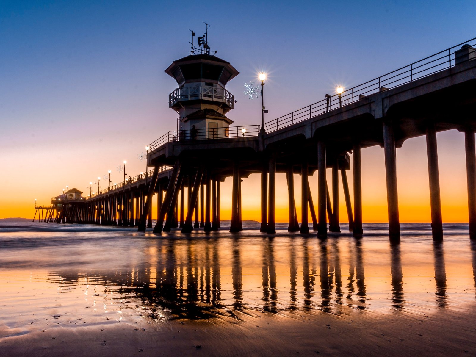 Huntington Beach Pier stretching into the Pacific at low tide, with the flat coastal plain of Huntington Beach and Pacific Coast Highway behind it.